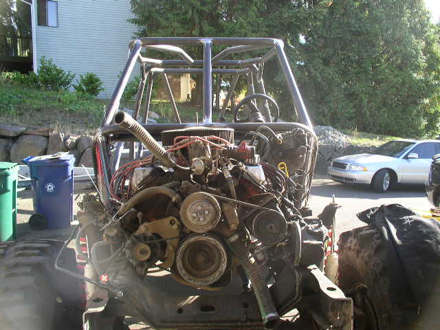 Tube-chassis off-road buggy with roll cage and exposed V8 engine, mid-build in a driveway.