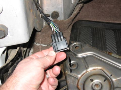 1995 Ford Bronco - A hand holds a black multi-pin electrical connector with several colored wires (blue, green, white, yellow) exiting a wrapped harness, posi…