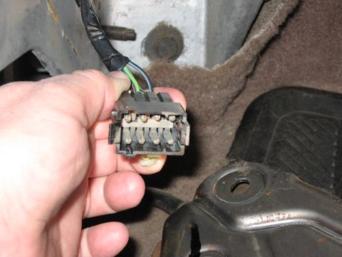 1995 Ford Bronco - A hand holds a gray multi-pin electrical connector with green, white, and blue wires wrapped in black tape, beneath a vehicle chassis. Meta…