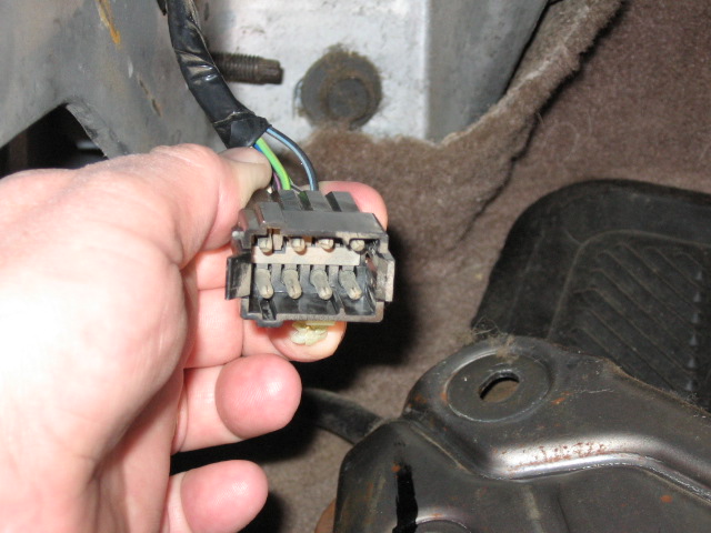 Hand holding gray multi-pin wiring connector under a vehicle chassis