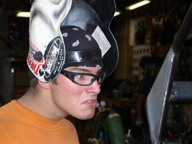 Man with flipped-up welding helmet and safety glasses in a fabrication shop