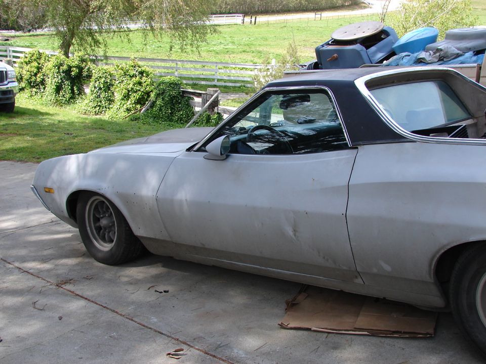 Side view of a light-colored Ford Ranchero with a black vinyl top. It's parked on a concrete driveway