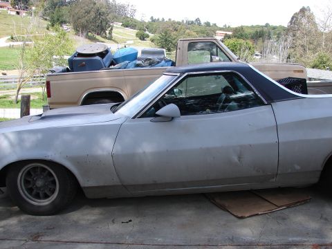 1973 Ford Ranchero - Primer-gray 1972 Ford Ranchero parked next to a tan pickup truck loaded with junk.