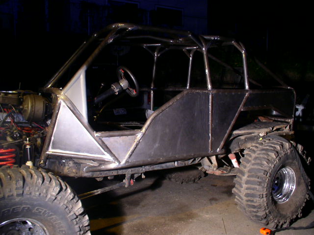 Bare-metal tube-chassis buggy under construction at night on large mud tires