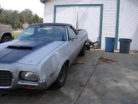 1973 Ford Ranchero - A 1973 Ford Ranchero sits in front of a garage, partially obscured by another vehicle.