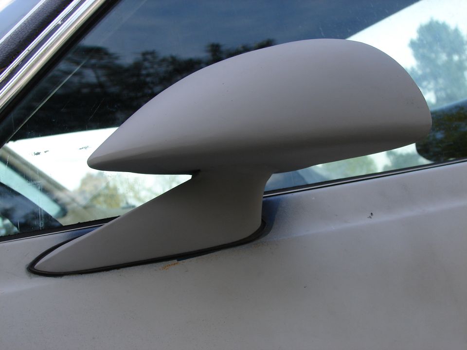 Gray primer side mirror mounted on a vehicle door, close-up
