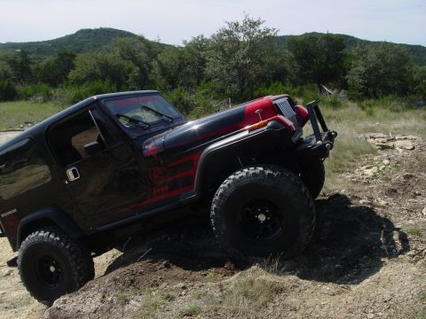 1973 Ford Bronco - A black Jeep Wrangler with red accents navigates a rocky, off-road path.