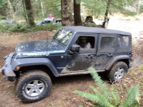 2005 Jeep Wrangler - A Jeep Wrangler navigates a muddy trail in a wooded area, with another vehicle in the distance.