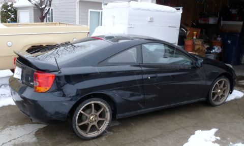 2006 Ford E350 - A black Toyota Celica GT is parked in a driveway during a snowfall, next to a tan pickup truck.