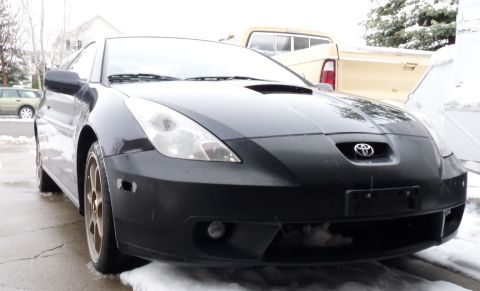 2006 Ford E350 - Low three-quarter front view of a black Toyota Celica coupe with flat-black front bumper and hood, no front plate, and bronze/gold multi-sp…