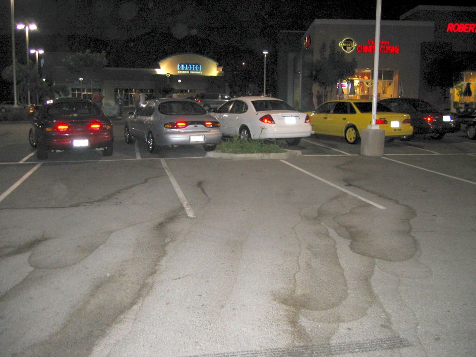 Cars angled in a parking lot at night in front of a Coffee shop and dealership