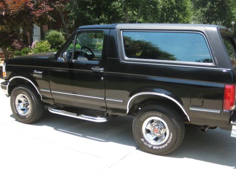 1992 Ford Bronco - This black 1992 Ford Bronco is shown from the side, parked on a paved surface in front of a residential building.