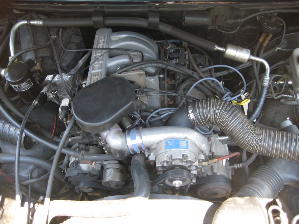 Engine bay with V8 engine, supercharger, and hoses. Supermotors.net logo visible