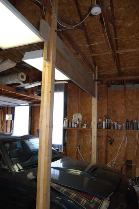 1985 Mercury Grand Marquis - Car parked inside a garage with overhead lighting and shelves stocked with bottles.