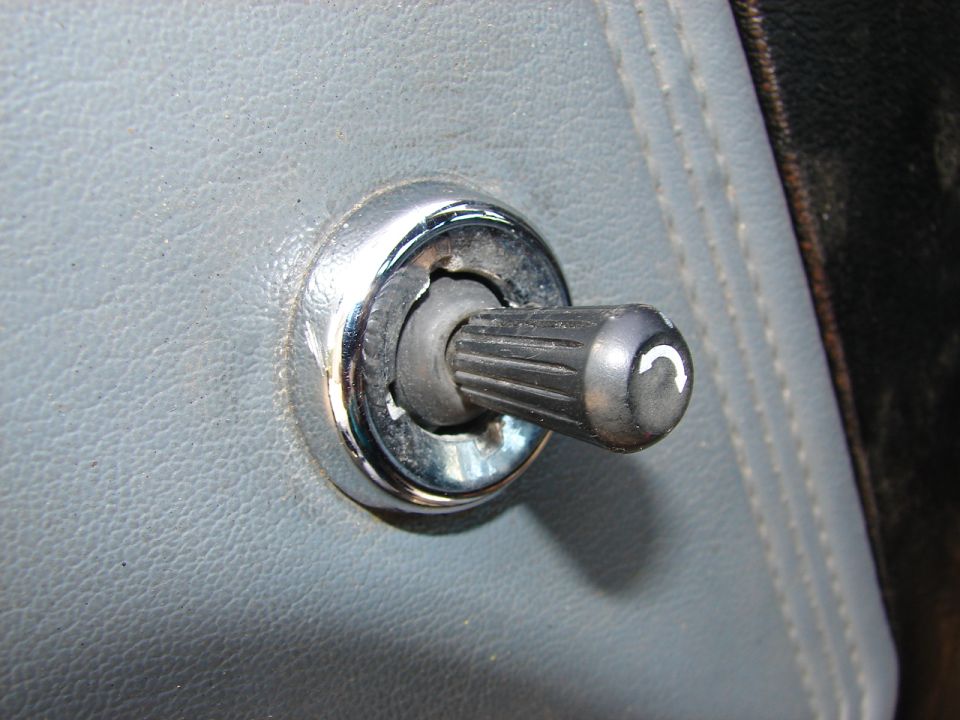 Close-up of a black ribbed door lock knob with a white curved arrow symbol on a gray textured surface