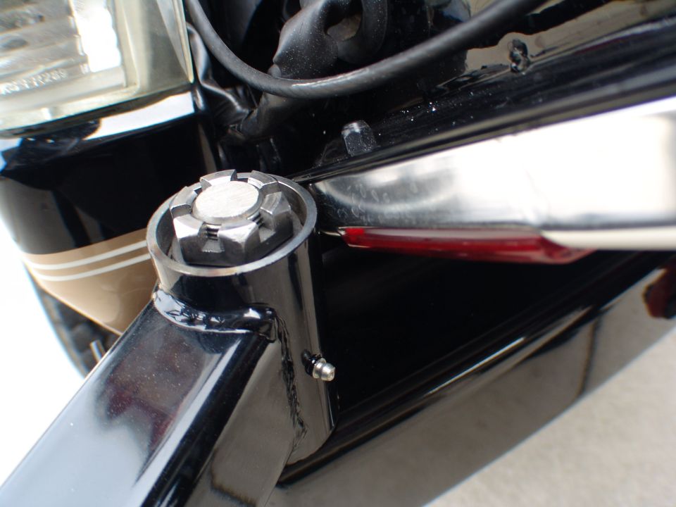 Close-up of vehicle's front corner, showing part of headlight, frame, and a decorative bolt