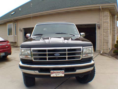 1996 Ford Bronco - The front grille and headlights of a black Ford Bronco are visible, parked in front of a garage.