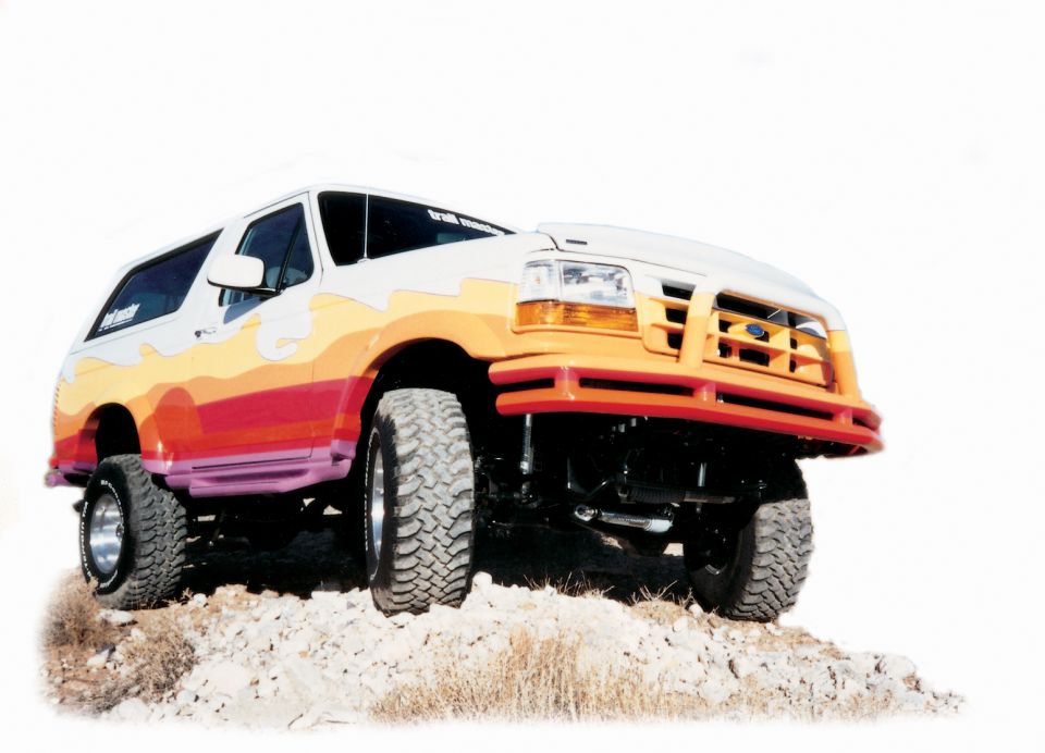 Lifted Ford Bronco with sunset flame paint and matching tube bumper posed on rocks