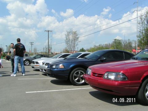 2007 Ford Mustang - A row of Ford Mustangs are parked in a lot, with the front end of a red 1993 model prominently displayed.
