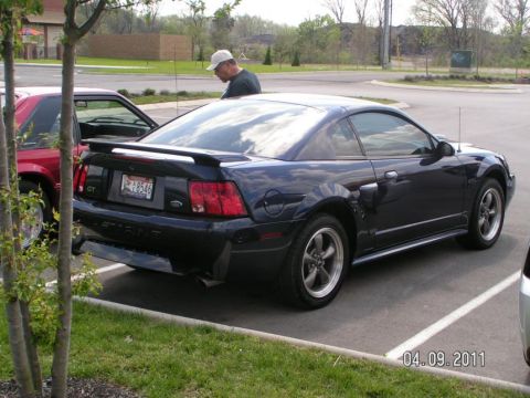 2007 Ford Mustang - A dark blue Ford Mustang coupe is parked in a lot next to a red car, with a man standing nearby.