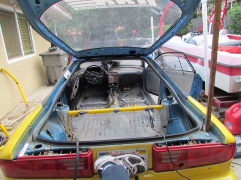 1995 Ford Probe - The interior of a car has been stripped down, revealing its frame and racing cage, with doors and trunk open.