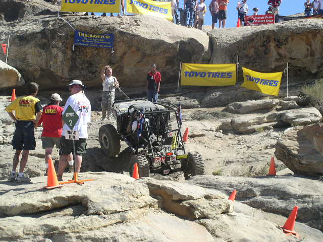 Off-road buggy climbing rocks with orange cones and Toyo Tires banners