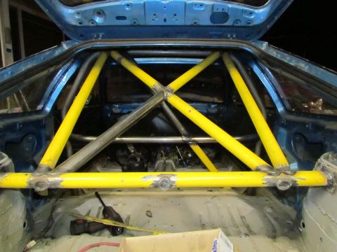1995 Ford Probe - The interior of a car shows a custom yellow roll cage installed, with the trunk area exposed.