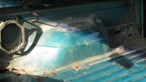 1992 Ford Bronco - The interior floor pan of a 1992 Ford Bronco shows significant rust and wear, with a speaker housing on the left side.