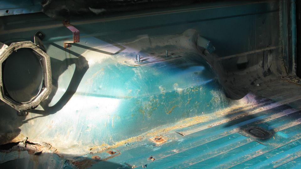 1992 Ford Bronco interior floor pan, teal, showing rust and wear. Speaker housing visible on left