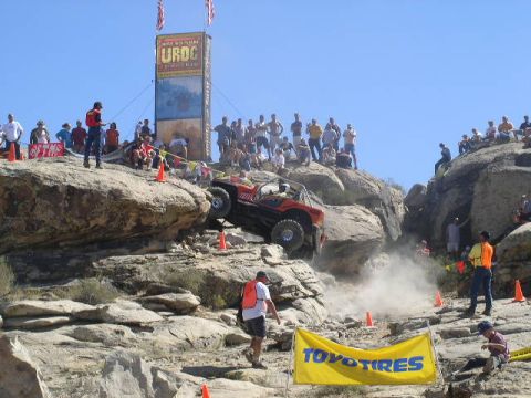 1979 Ford Bronco - An off-road buggy navigates a challenging rocky terrain during an event, with a crowd observing from the surrounding hills.