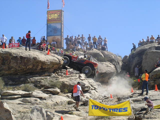 Off-road buggy going up a rocky hill with spectators watching. A "Toyo Tires" banner is in the foreground