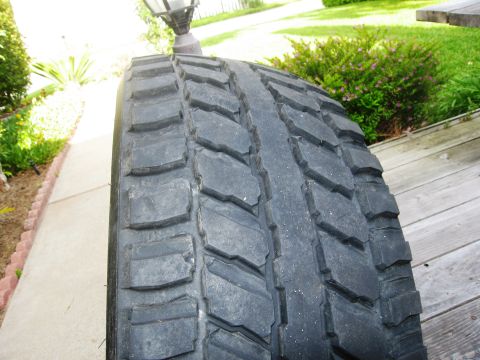 1986 Ford Bronco - A close-up view of a tire tread, with a sidewalk and greenery in the background.