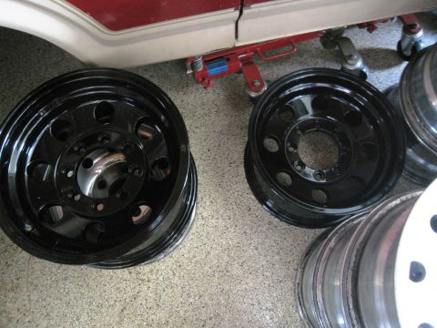 1986 Ford Bronco - Several black off-road wheels are stacked on the ground, with a vehicle and jack visible above.