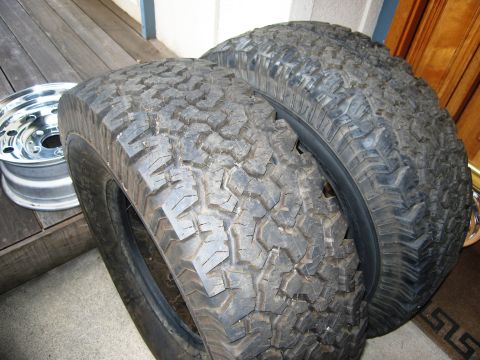 1986 Ford Bronco - A pair of aggressive tread off-road tires and a single chrome wheel are displayed, likely for sale or as spare parts.