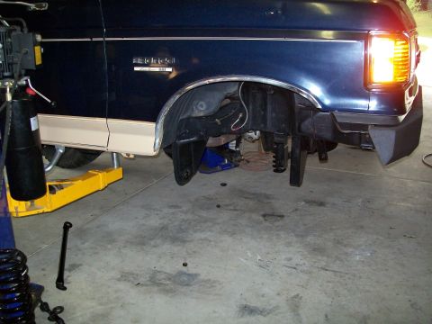1990 Ford Bronco - The front driver side wheel well of a 1990 Ford Bronco is visible as the vehicle is lifted for maintenance.