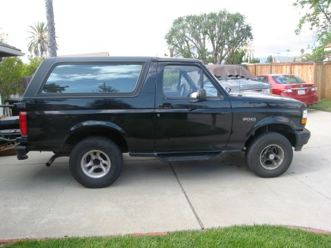 1986 Ford Bronco - Side profile of a black 1986 Ford Bronco parked on a driveway.