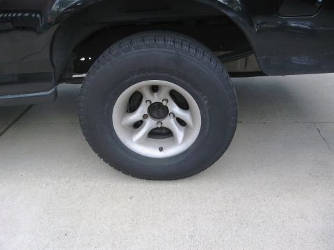 1986 Ford Bronco - Close-up view of a black vehicle's rear wheel and tire, showing the alloy rim and tire tread.