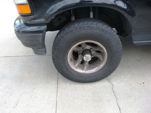 1986 Ford Bronco - Close-up of a black SUV's front wheel and fender area, showing the tire and rim.