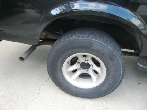 1986 Ford Bronco - Close-up of a black SUV's rear wheel and exhaust pipe.