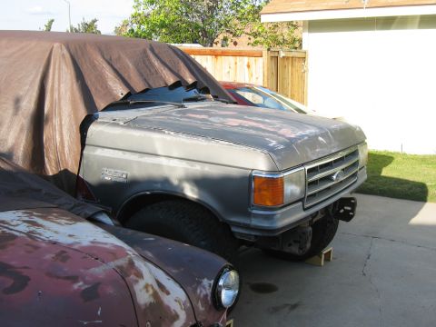 1986 Ford Bronco - The front clip of a 1987-1991 Ford Bronco is visible, with the rest of the vehicle covered by a tarp. Another vehicle is parked in front.