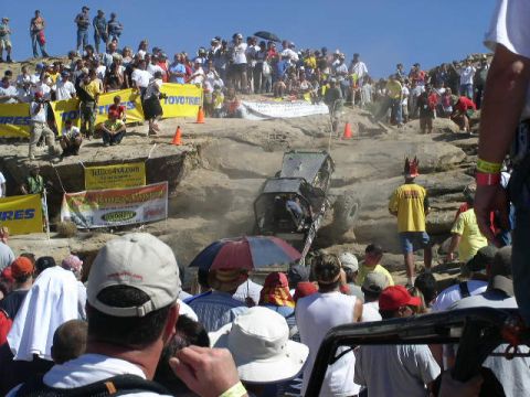1979 Ford Bronco - A crowd watches an off-road vehicle navigate a challenging rocky obstacle course under a clear blue sky.