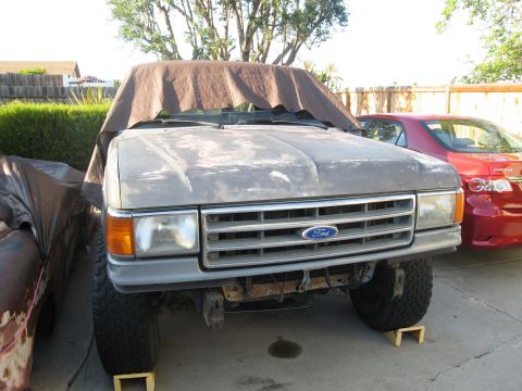 1986 Ford Bronco - A Ford truck is parked in a driveway, partially covered by a tarp, with another vehicle beside it.
