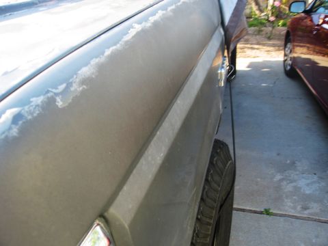 1986 Ford Bronco - The side panel of a vehicle shows significant paint damage, with another car parked closely beside it.