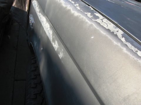 1986 Ford Bronco - Close-up view of the side of a gray vehicle showing damage and peeling paint on the fender and door panel.