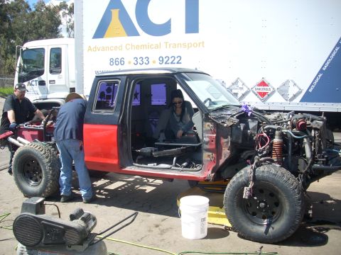 1992 Ford Ranger - Two people work on a disassembled truck, with a large transport truck behind it.