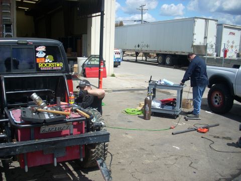 1992 Ford Ranger - Two men working on vehicles outside a garage with large trailers in the background.