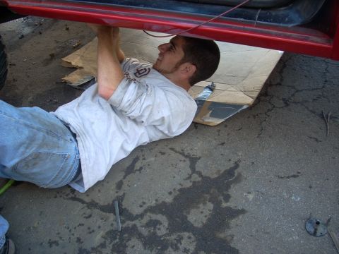 1992 Ford Ranger - A person works on the undercarriage of a red vehicle, lying on the ground with cardboard underneath.