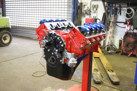 1973 Ford Ranchero - A V8 engine, painted red and black with blue valve covers, is mounted on a stand in a workshop.