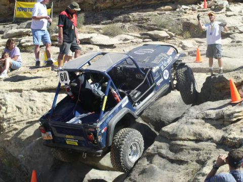1979 Ford Bronco - A blue off-road buggy navigates a challenging rocky course, with spectators watching from the sidelines.