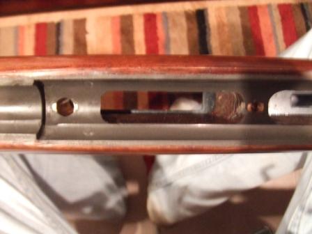 1996 Ford Bronco - Detail of a rifle's receiver and wooden stock, with a glimpse of a striped rug and legs in jeans.